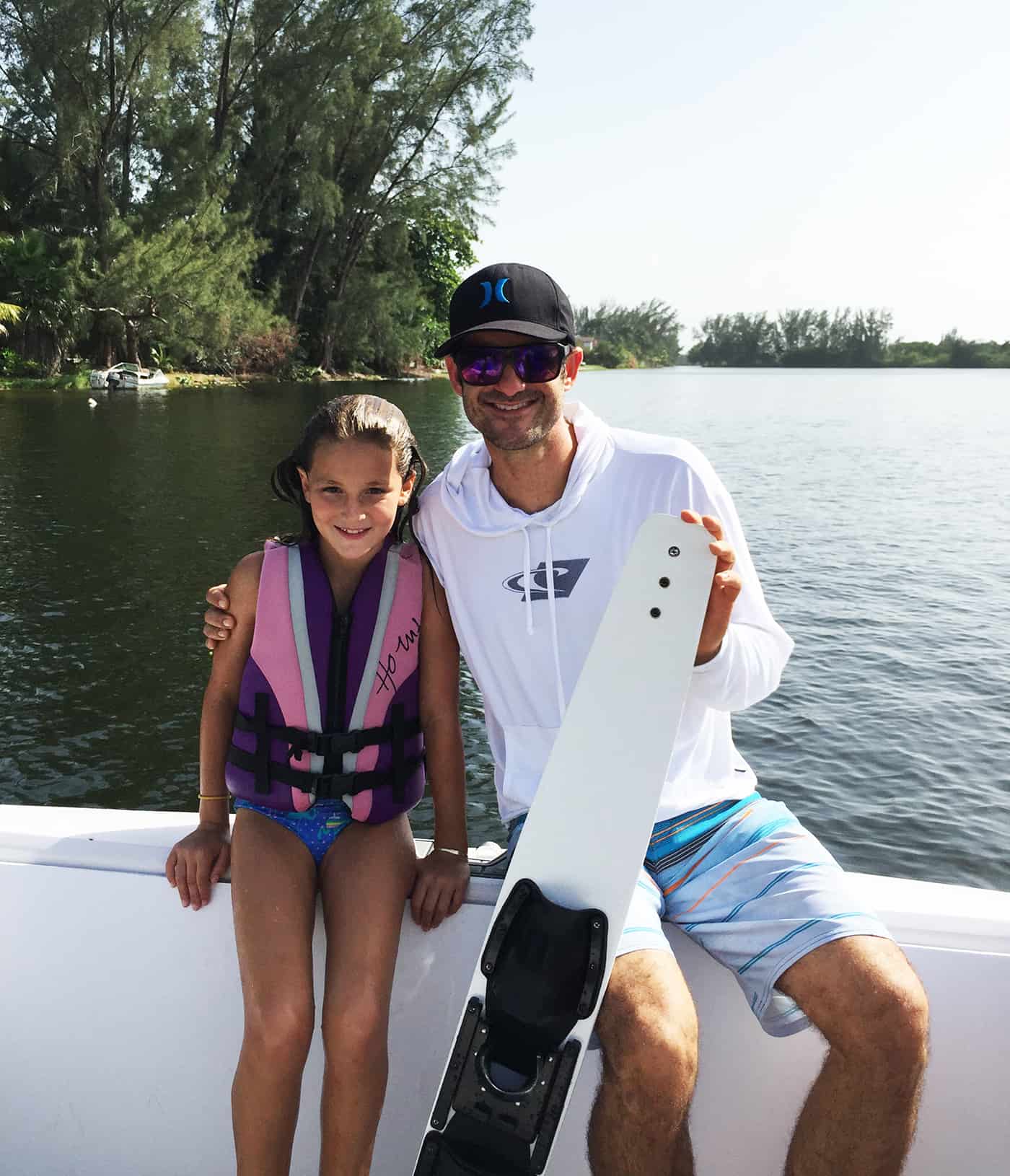 man and little girl sitting on edge of boat holding a white ski