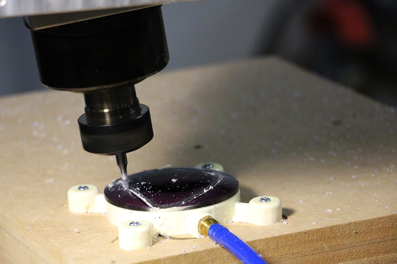 5 axis machine cutting out a purple lens shape for sunglasses