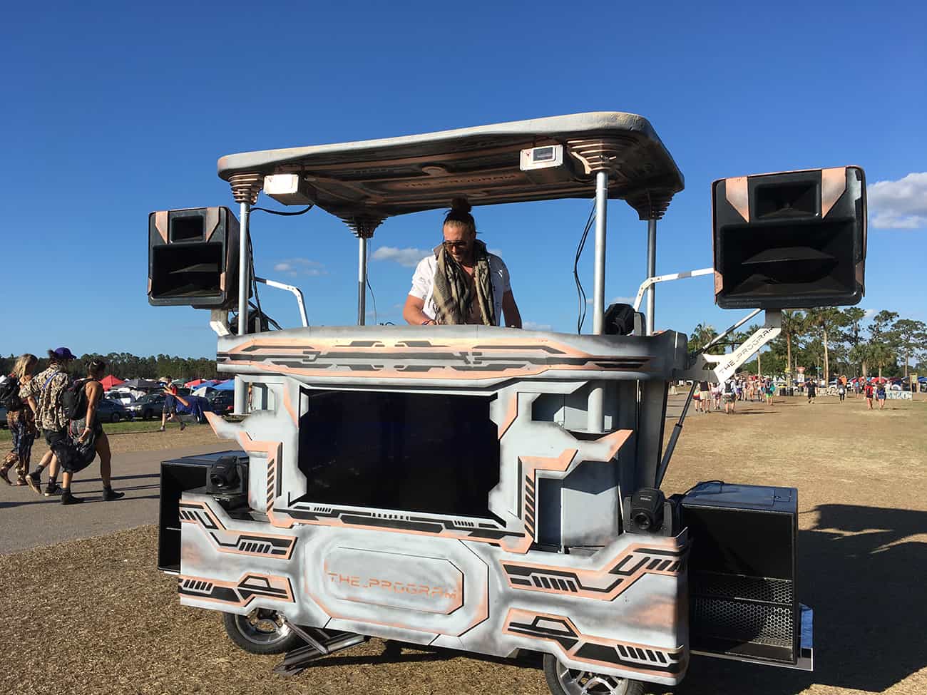 man playing music in the daytime off a custom fabricated golf cart with speakers, amps and a tv.